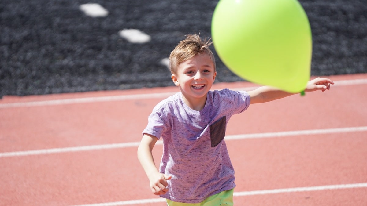 boy in purple shirt chasing green balloon on track field